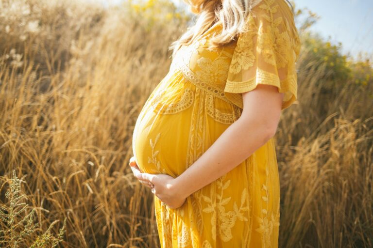A pregnant woman in yellow dress holding her belly adorably standing against an ochre background of a grassland
