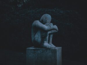 A stone statue of a human sitting in fetal position looking sad and dejected