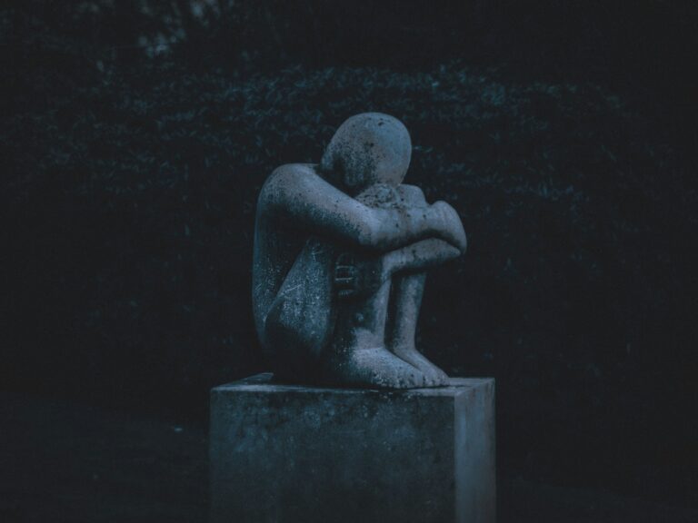 A stone statue of a human sitting in fetal position looking sad and dejected